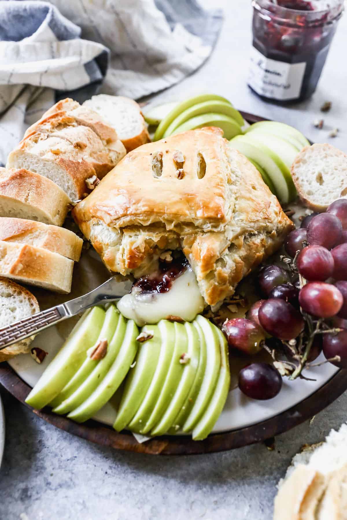 Baked Brie puff pastry on a platter surrounded by apples, grapes, and bread.