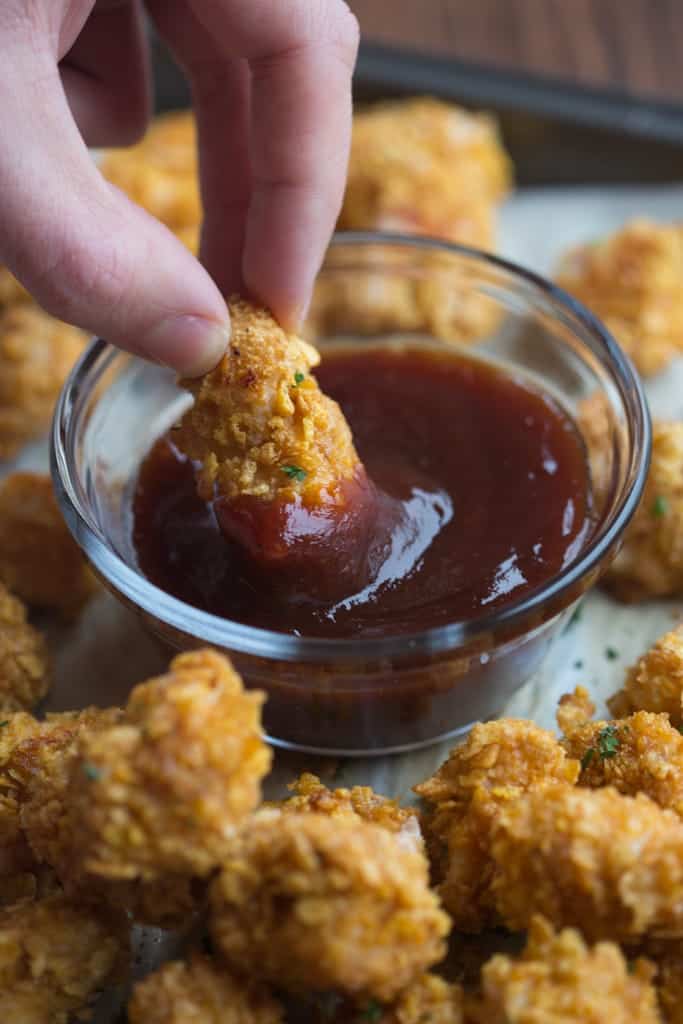 A hand dipping Homemade BAKED Popcorn Chicken in BBQ sauce.