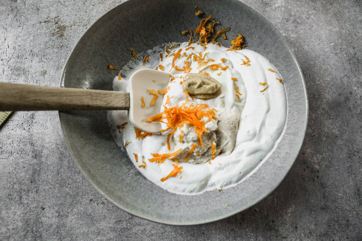 A bowl with orange zest, dijon mustard, horseradish, and sour cream being folded into whipped cream.