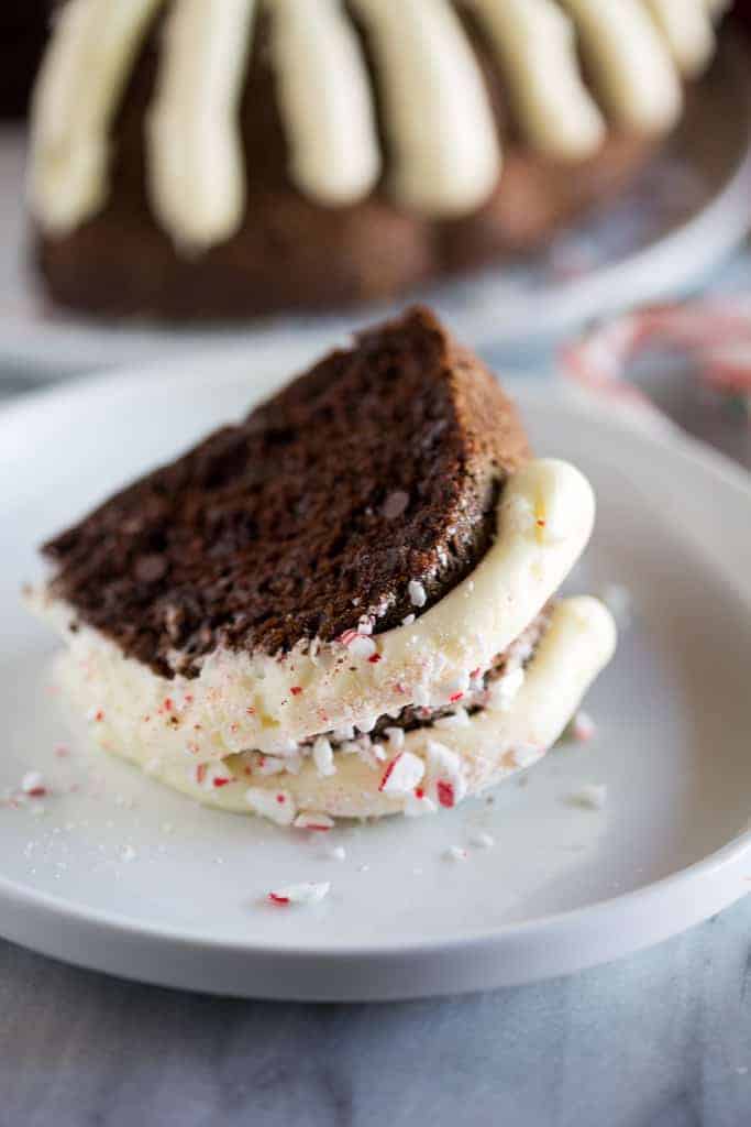 A slice of chocolate bundt cake with cream cheese frosting and crushed candy canes laying on a white plate.