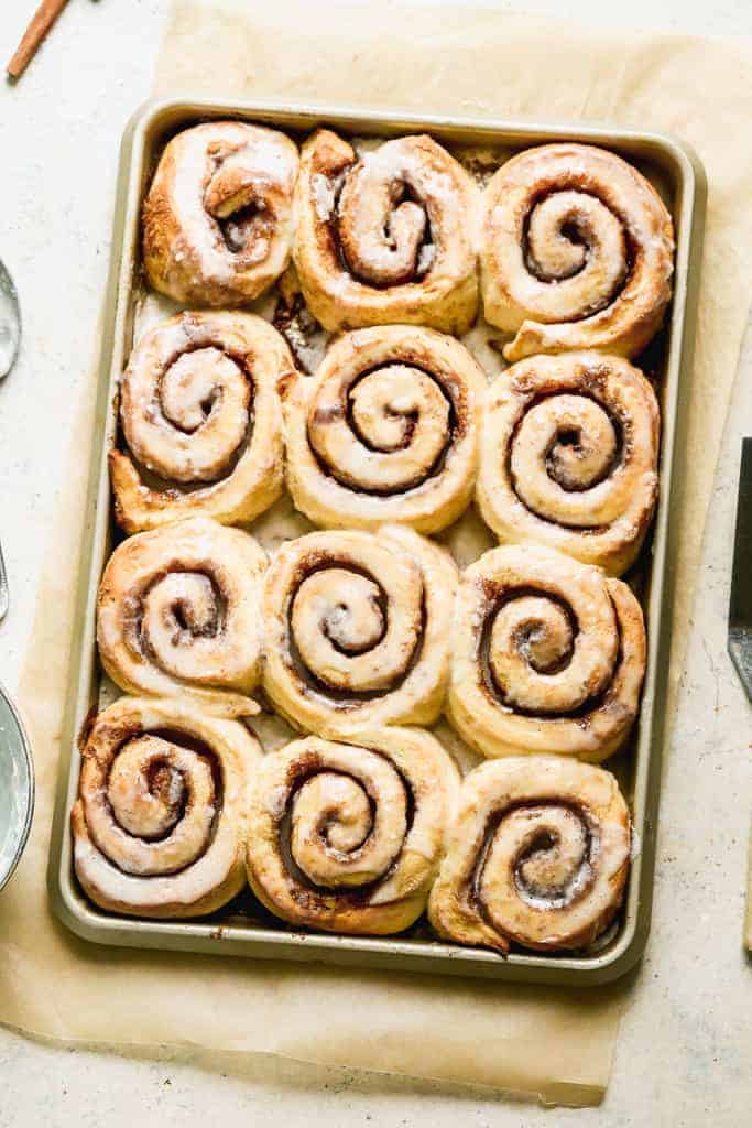 A sheet pan with 12 freshly baked cinnamon rolls with glaze on top.