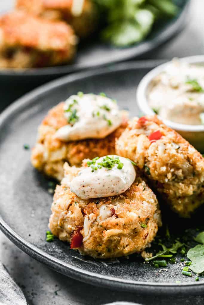 Three crab cakes on a plate with crab cakes sauce on top.