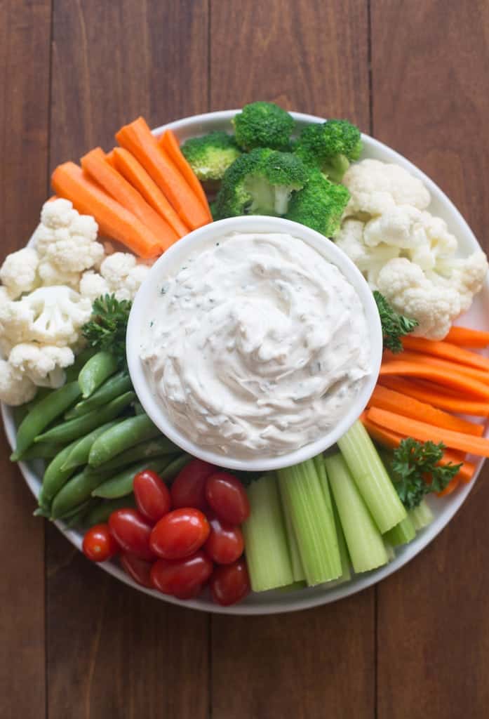 A circular tray filled with vegetables (tomatoes, carrots, broccoli, cauliflower, celery, snap peas) with an easy vegetable dip in the center.