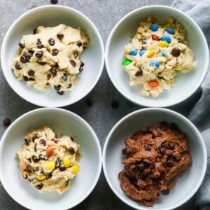Four bowls with different flavors of edible cookie dough in them including chocolate chip, peanut butter, chocolate, and M&M cookie dough.
