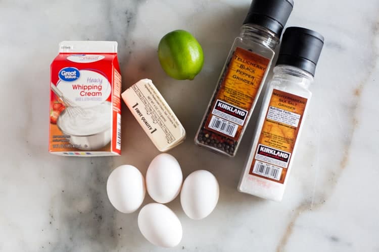 Overhead view of the ingredients needed for hollandaise sauce including butter, eggs, cream, lime juice, salt and pepper.