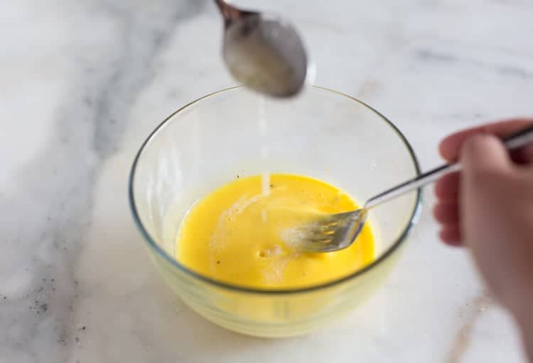 A spoonful of melted butter being added to a beaten egg yolk mixture to make hollandaise sauce.