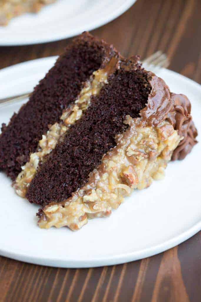 A slice of German Chocolate Cake served on a plate, with two layers of chocolate cake, and German chocolate frosting.