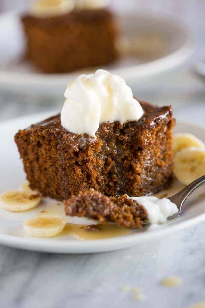 Gingerbread cake with a bite taken out of it, served on a plate with sliced bananas and vanilla cream sauce.