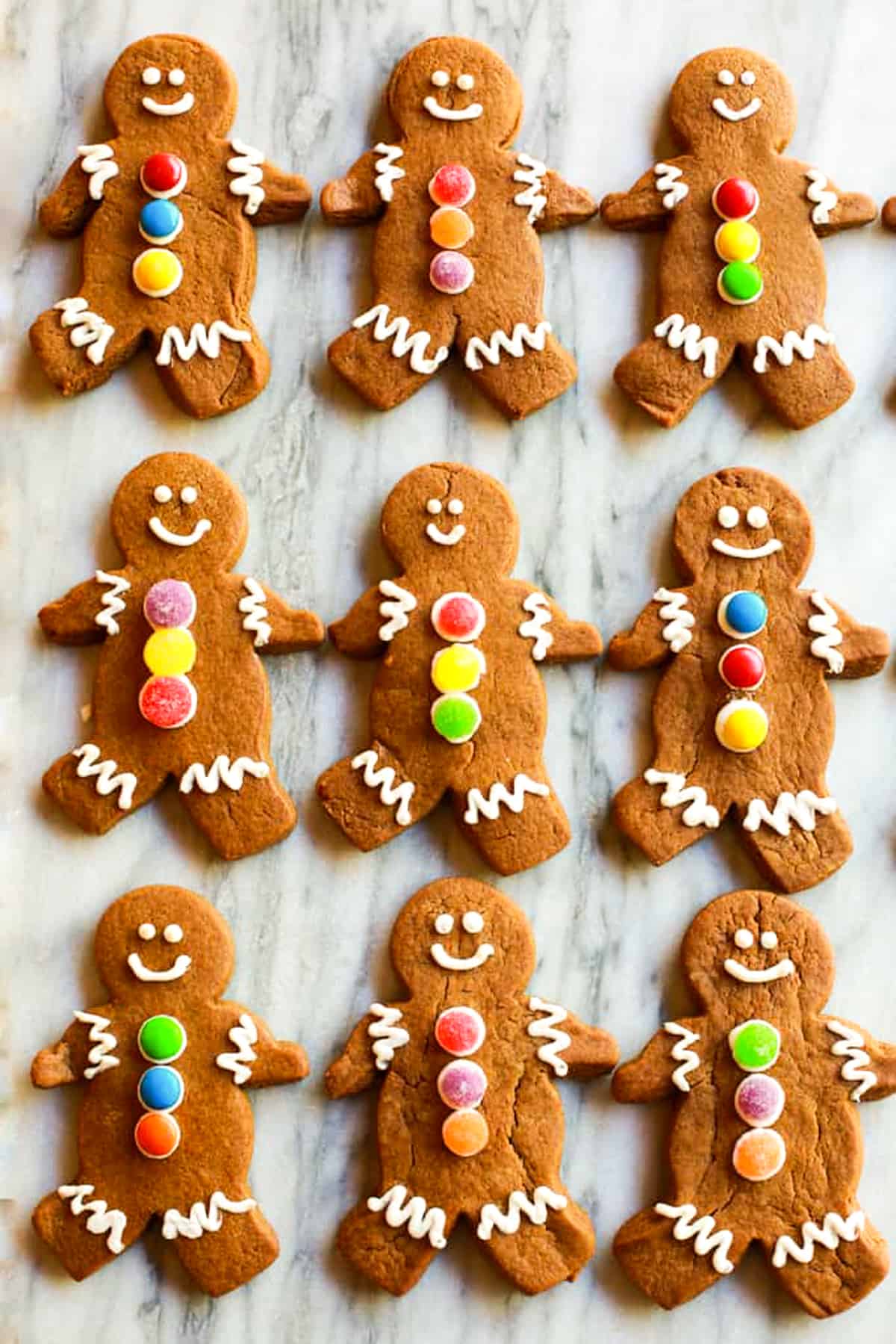 Nine gingerbread cookies decorated with faces and gumdrops, lined up in three rows.