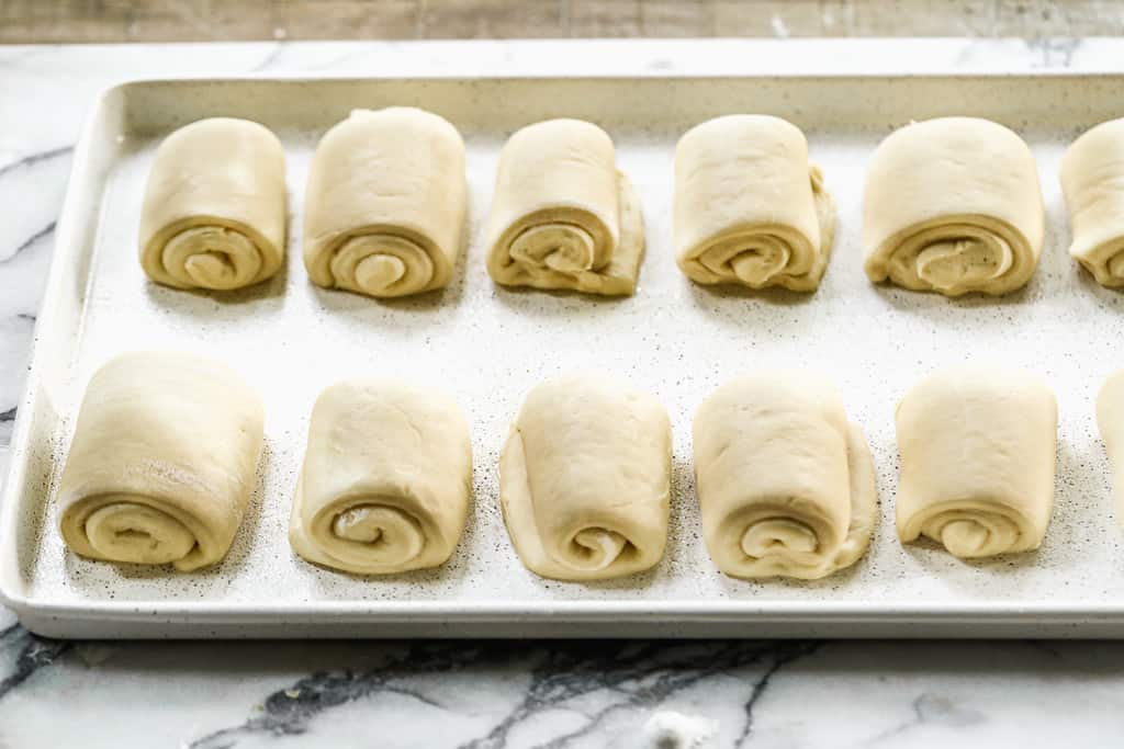 A sheet pan with risen dinner roll dough rolls ready to bake.