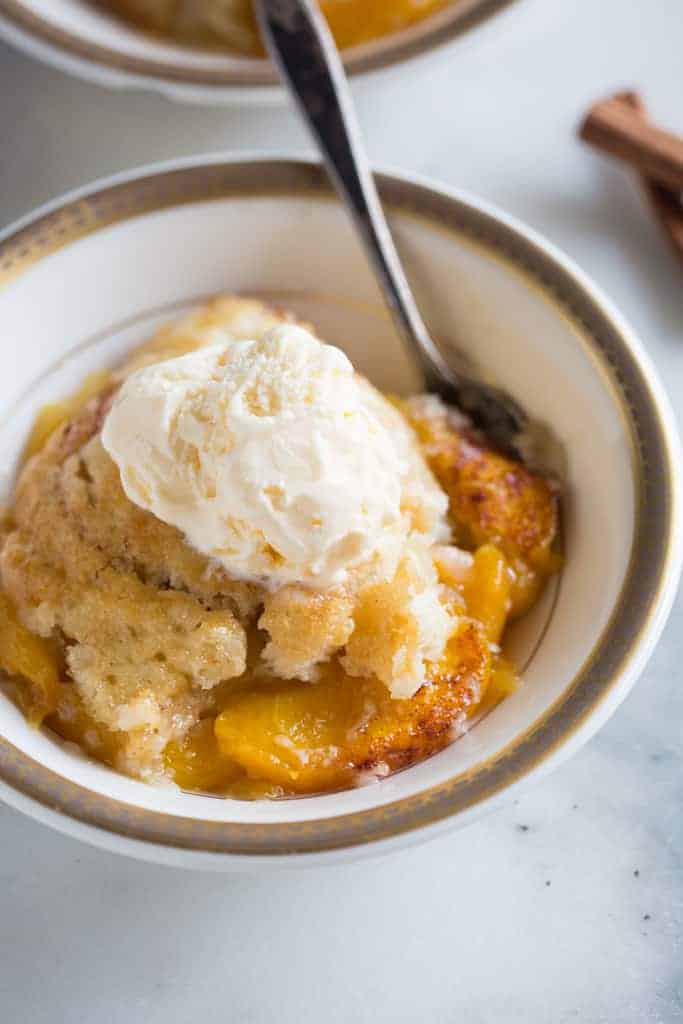 Peach cobbler served with a scoop of vanilla ice cream on top, in a bowl with a spoon.