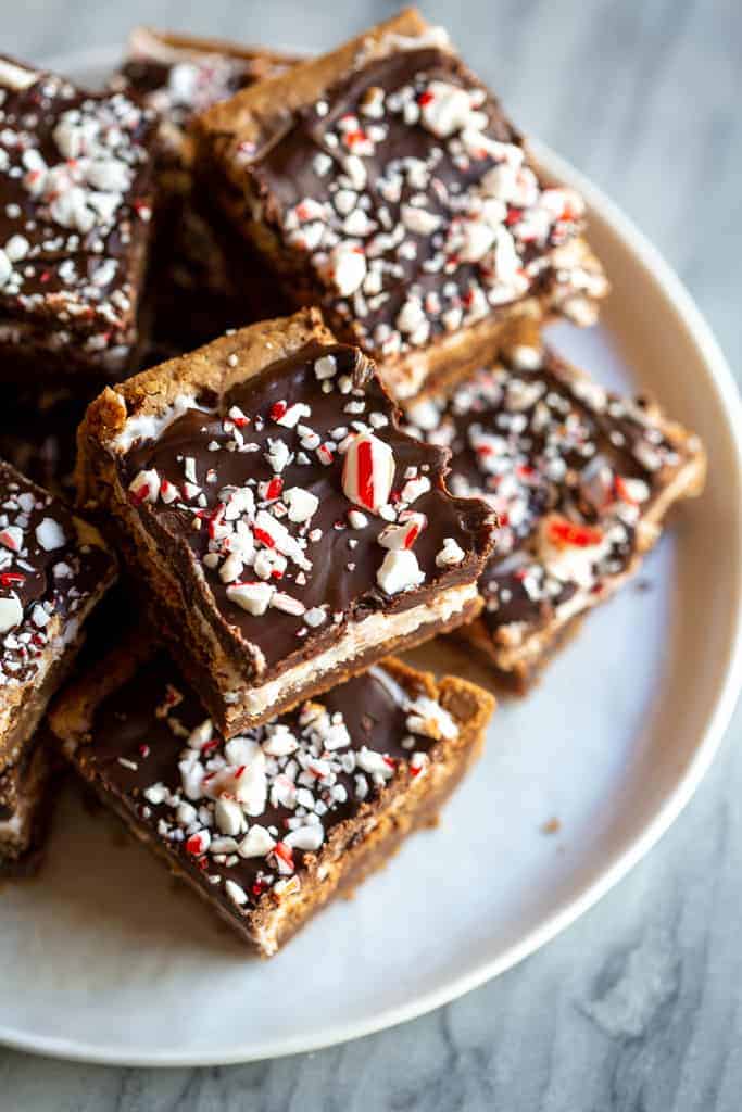 Peppermint Brownie squares with chocolate frosting and crushed candy canes on a white plate.