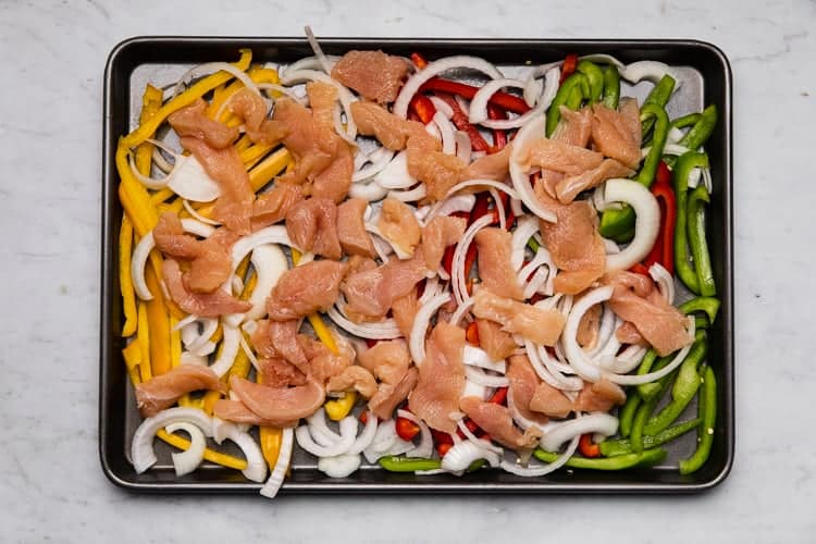 A sheet pan with chicken, bell pepper and onion sliced into strips.