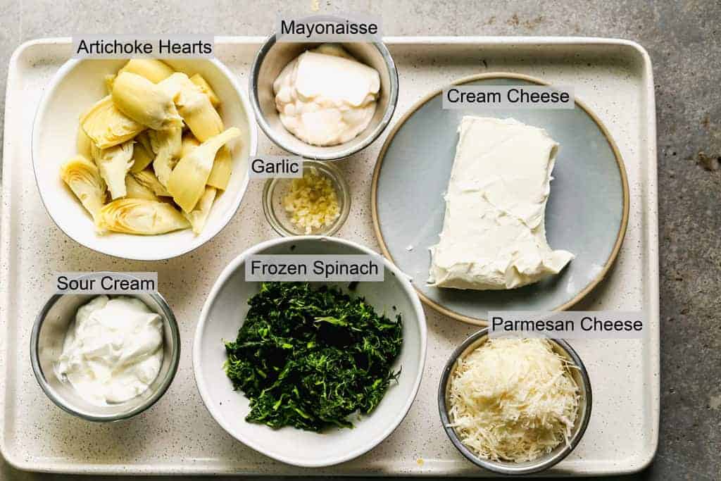 The ingredients needed to make Spinach Artichoke Dip labeled on a tray.