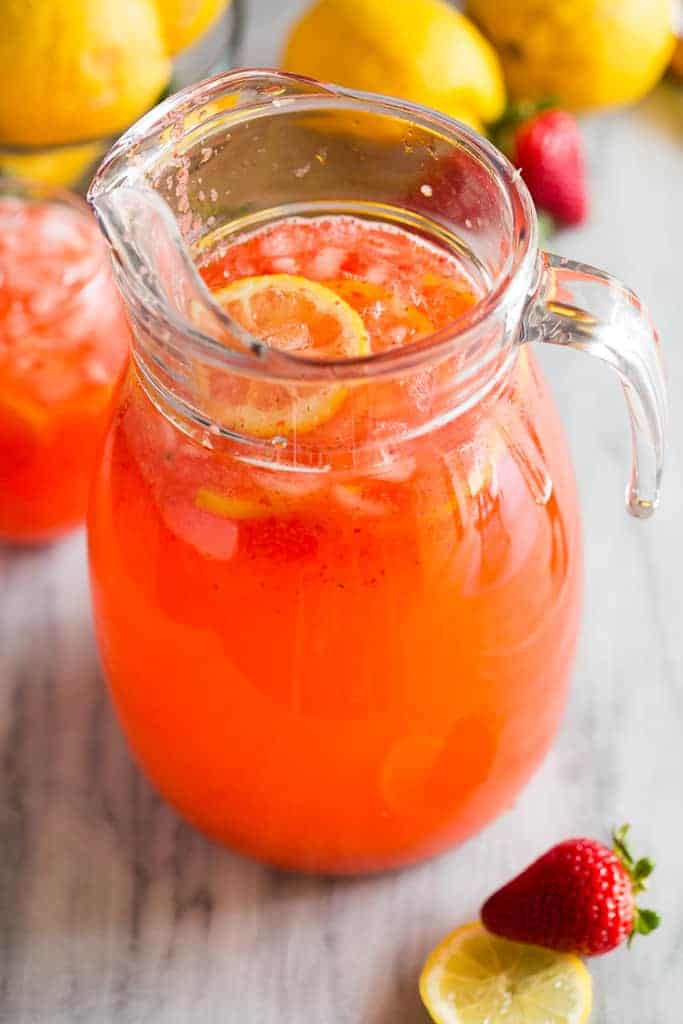 A clear glass pitcher with strawberry lemonade and lemon slices floating on top.