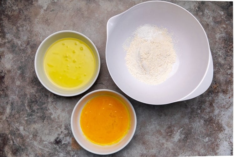 Egg whites in a mixing bowl, egg yolks in a separate mixing bowl, and flour, baking powder and salt in a third mixing bowl.